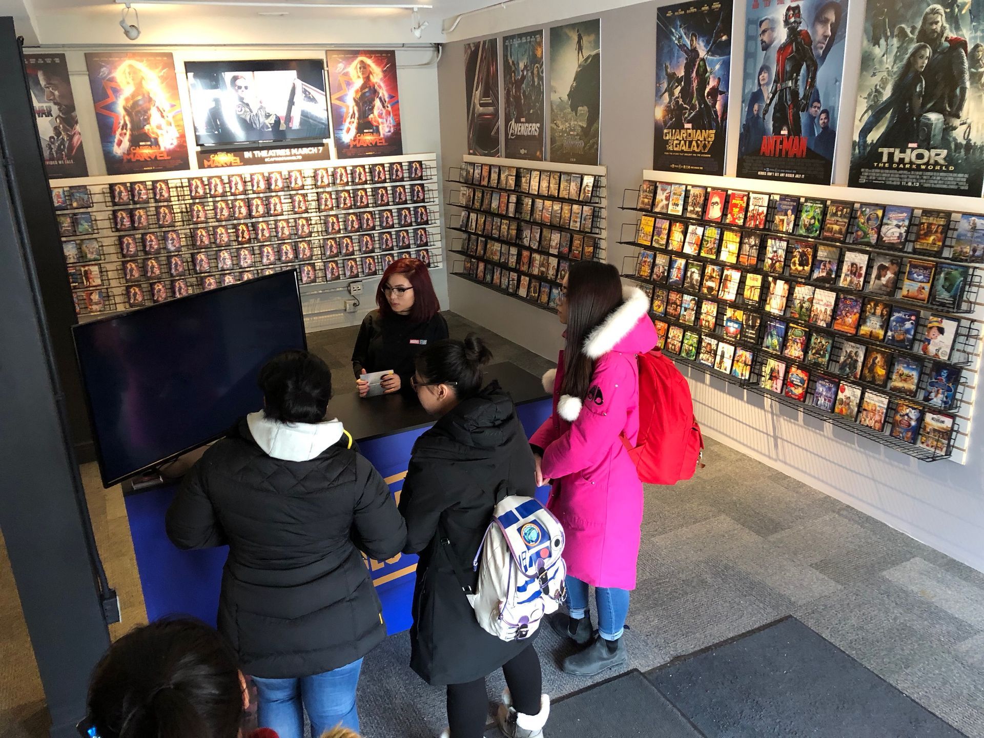 A group of people are standing in a room with posters on the wall.