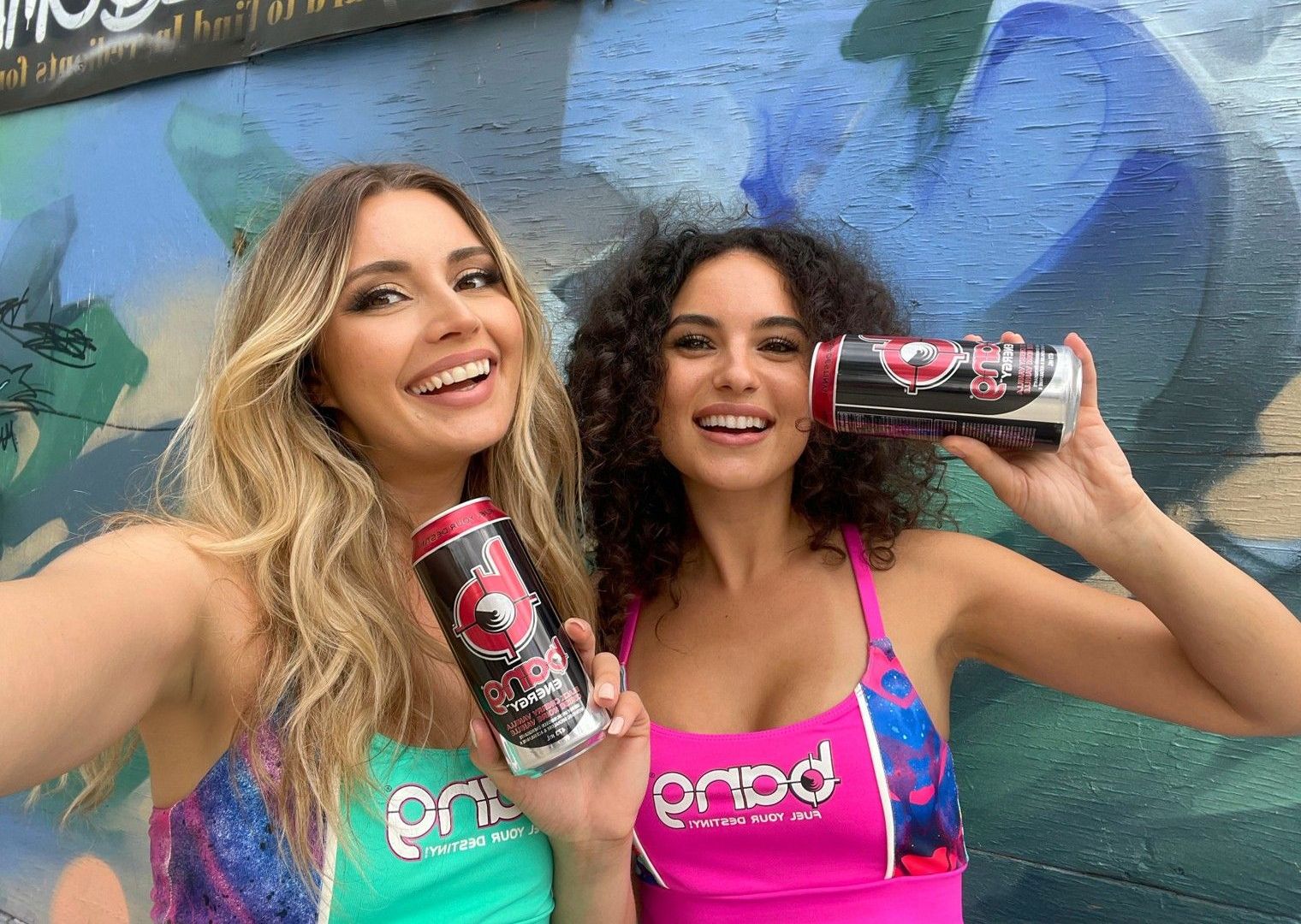 Two women are standing next to each other holding cans of soda.