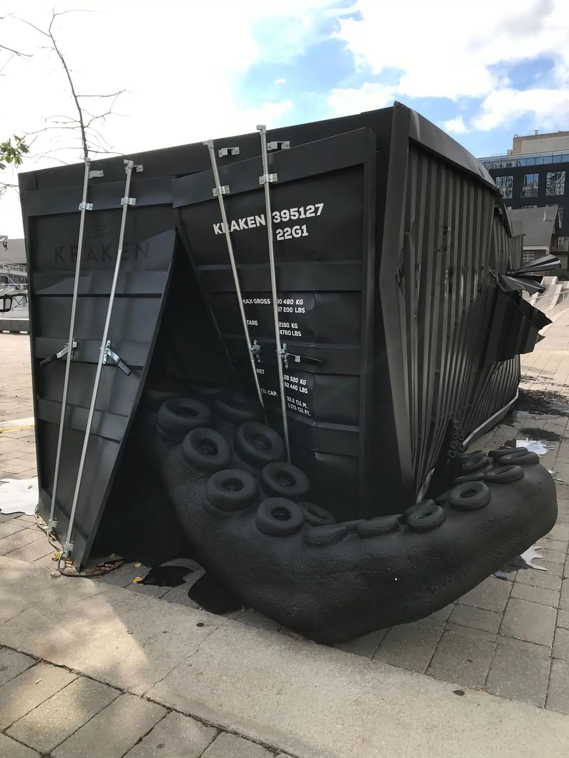 A black dumpster is sitting on the sidewalk next to a large tire.