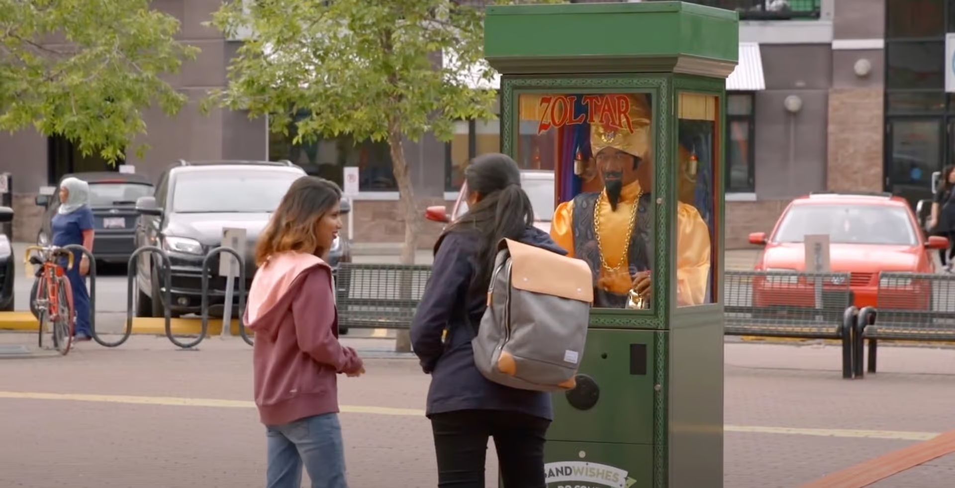 Two women are standing next to a green booth on a city street.