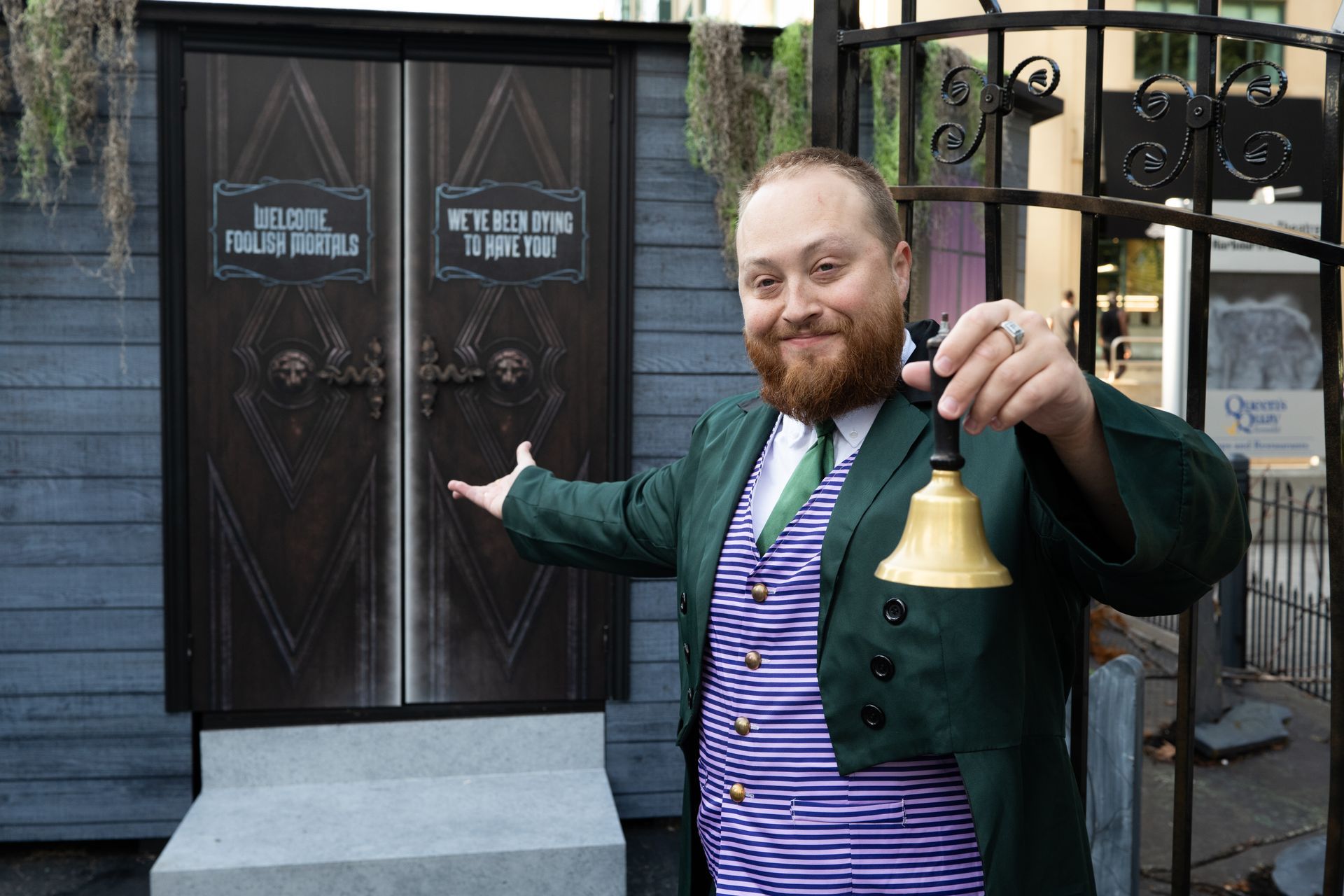 A man with a beard is holding a bell in front of a door.