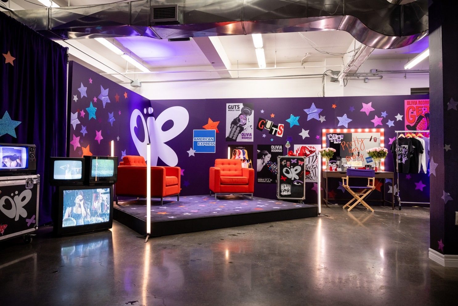 A room with a stage , chairs , televisions and a mirror.