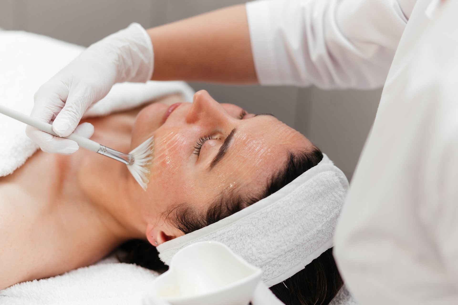 Person receiving a chemical facial peel, performed by gloved hands in a spa setting.