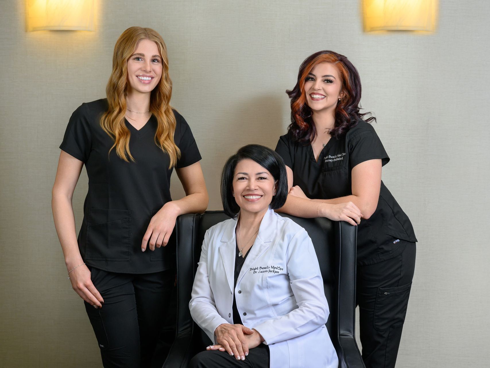Three women in scrubs are posing for a picture . one of the women is sitting in a chair.