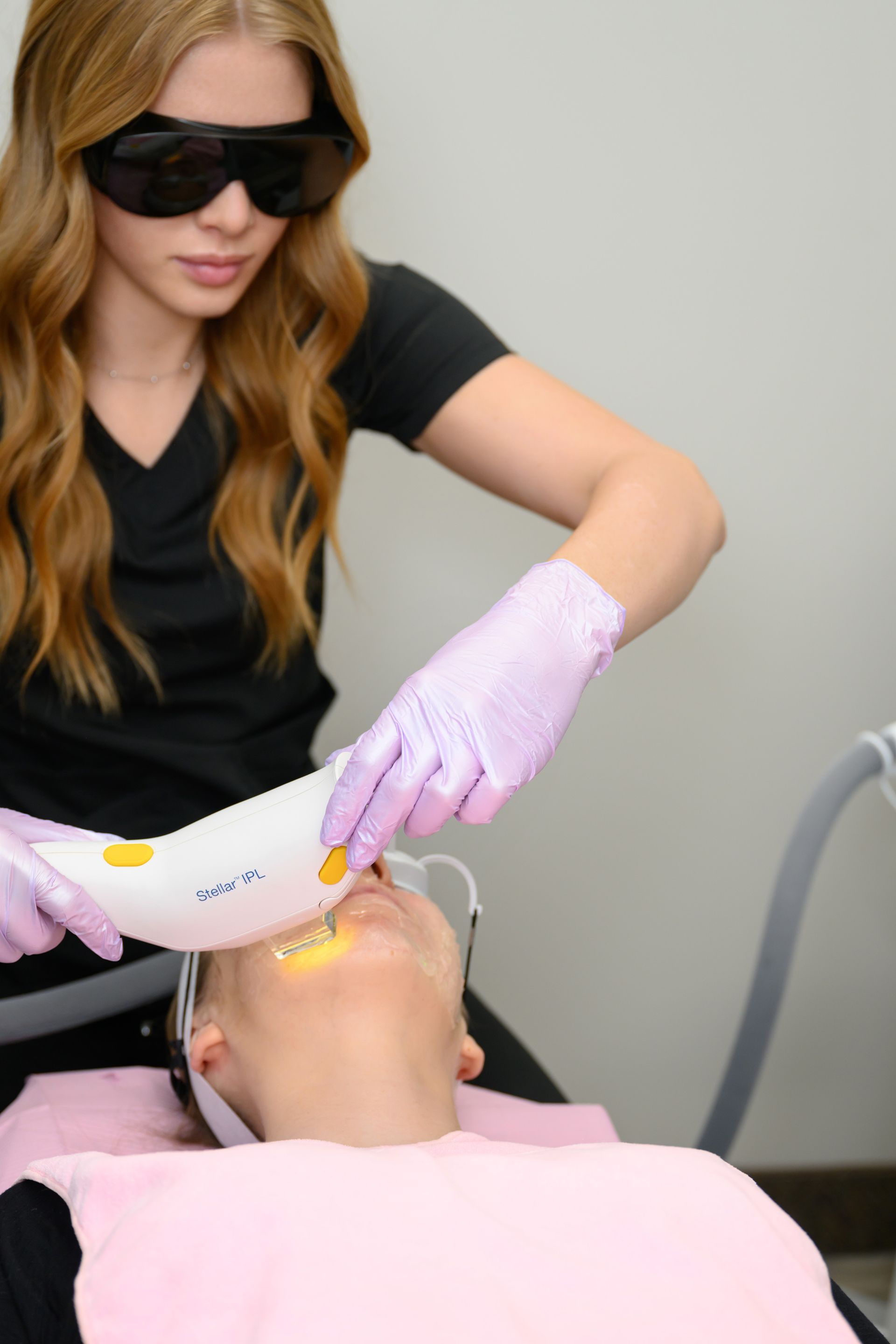 A woman wearing sunglasses is using a machine on a woman 's face.