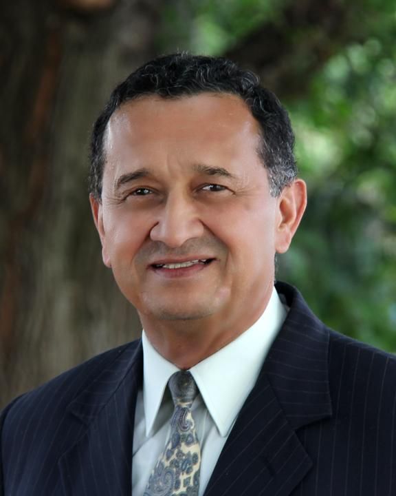 A woman is sitting at a desk with a laptop and a vase of flowers.