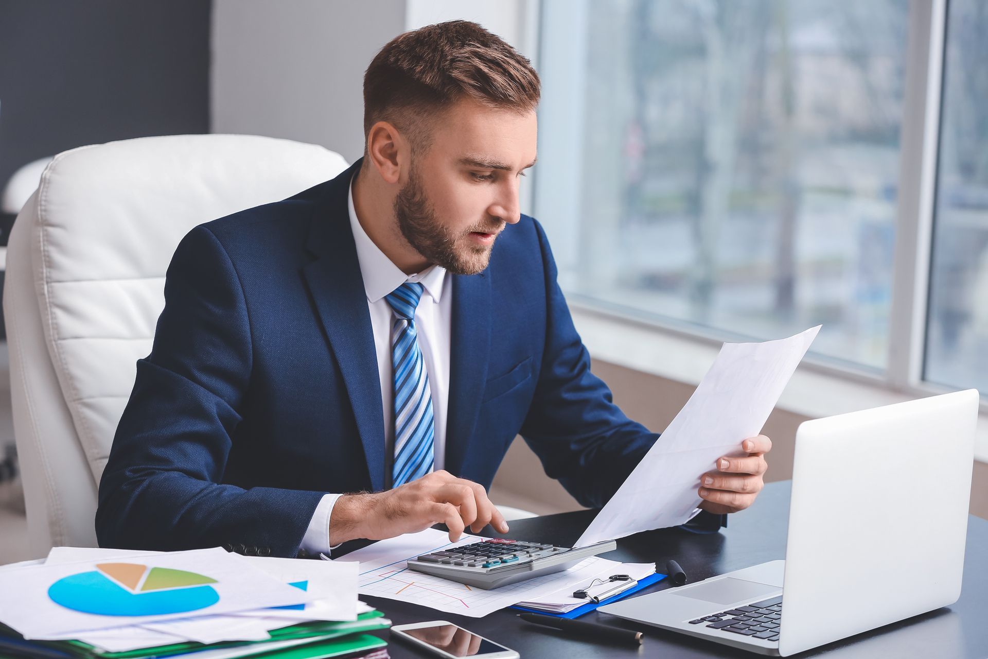 A male accountant, in a suit, is working in an office, using a calculator for accounting services.