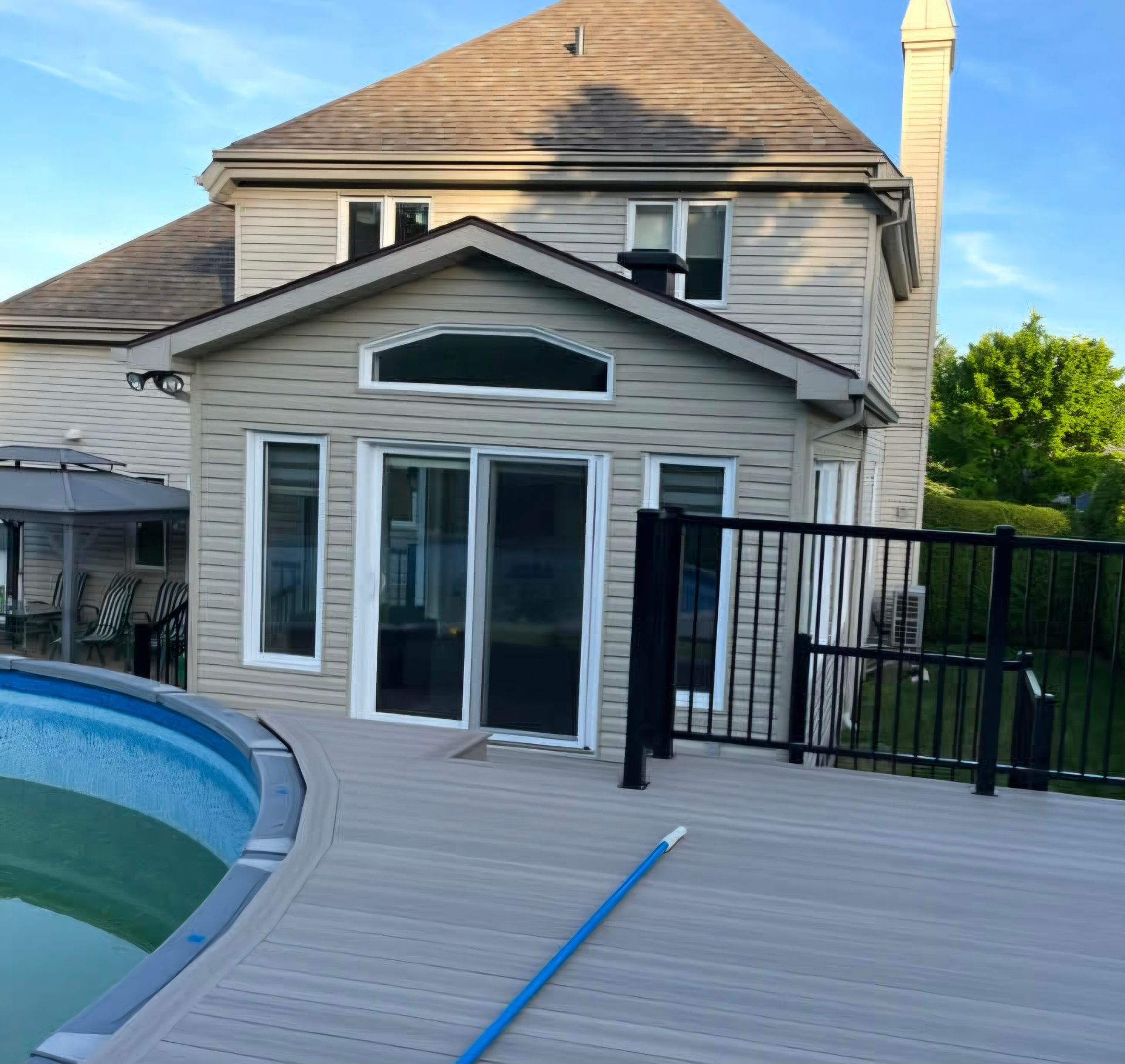 Une maison beige avec une véranda, dotée de portes coulissantes en verre et d'une terrasse donnant sur une piscine.