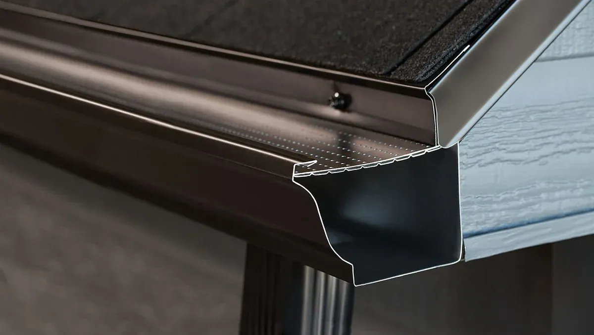 Gros plan sur une gouttière en métal foncé installée le long du bord d'un toit recouvert de bardeaux noirs.