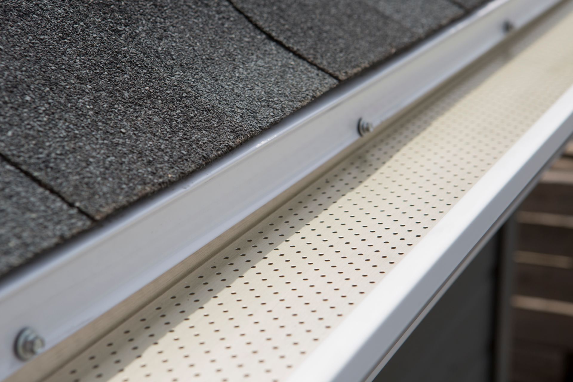 Gros plan d'une protection de gouttière en métal blanc installée sur un toit résidentiel en bardeaux d'asphalte.