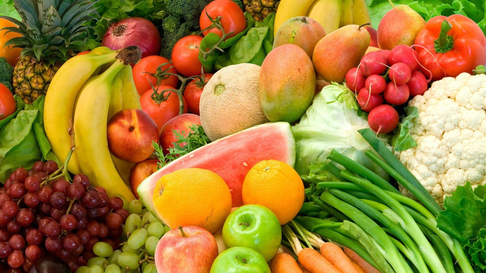 Assortment of colorful fruits and vegetables: bananas, grapes, tomatoes, oranges, carrots, cauliflower.