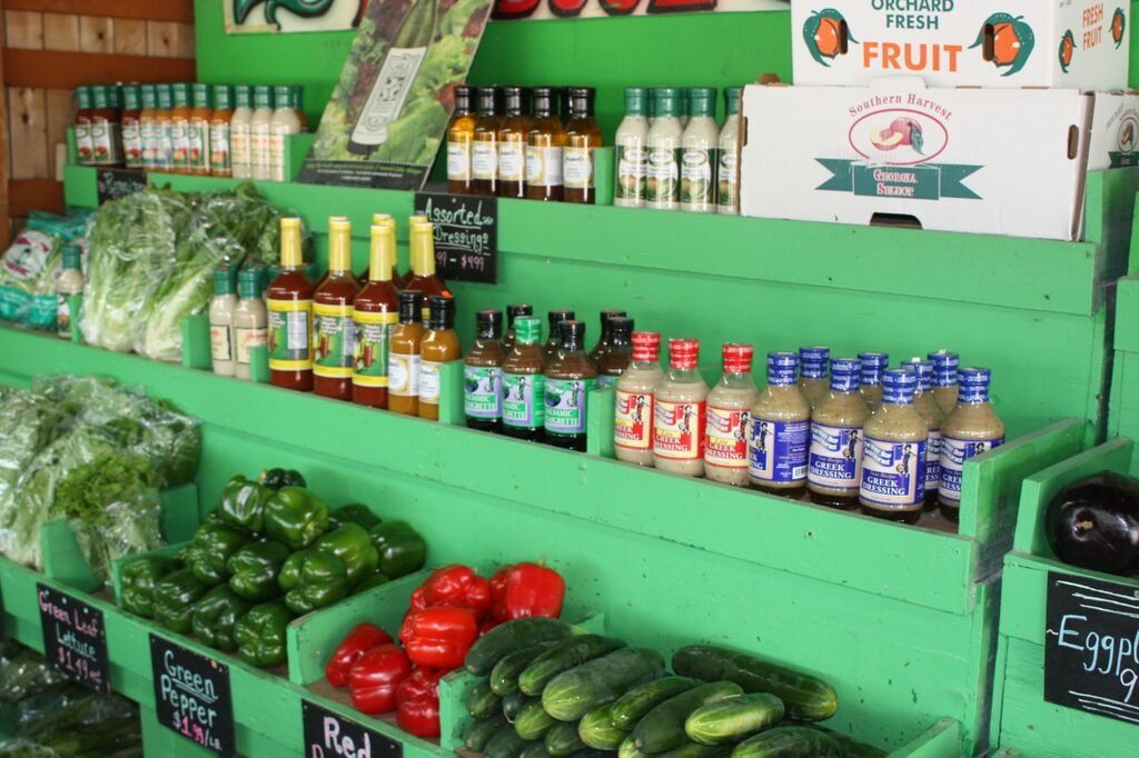 Green-painted farm stand display of produce, sauces, and a 