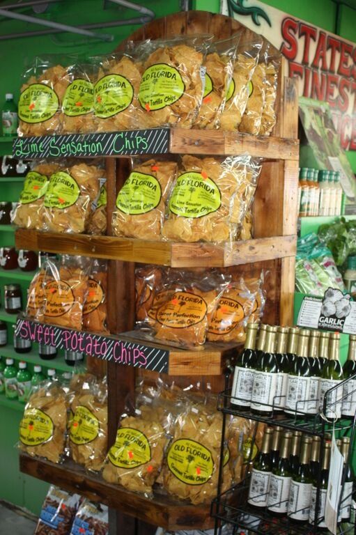 Wooden shelf displays bags of chips and bottles of wine in a green-walled store.