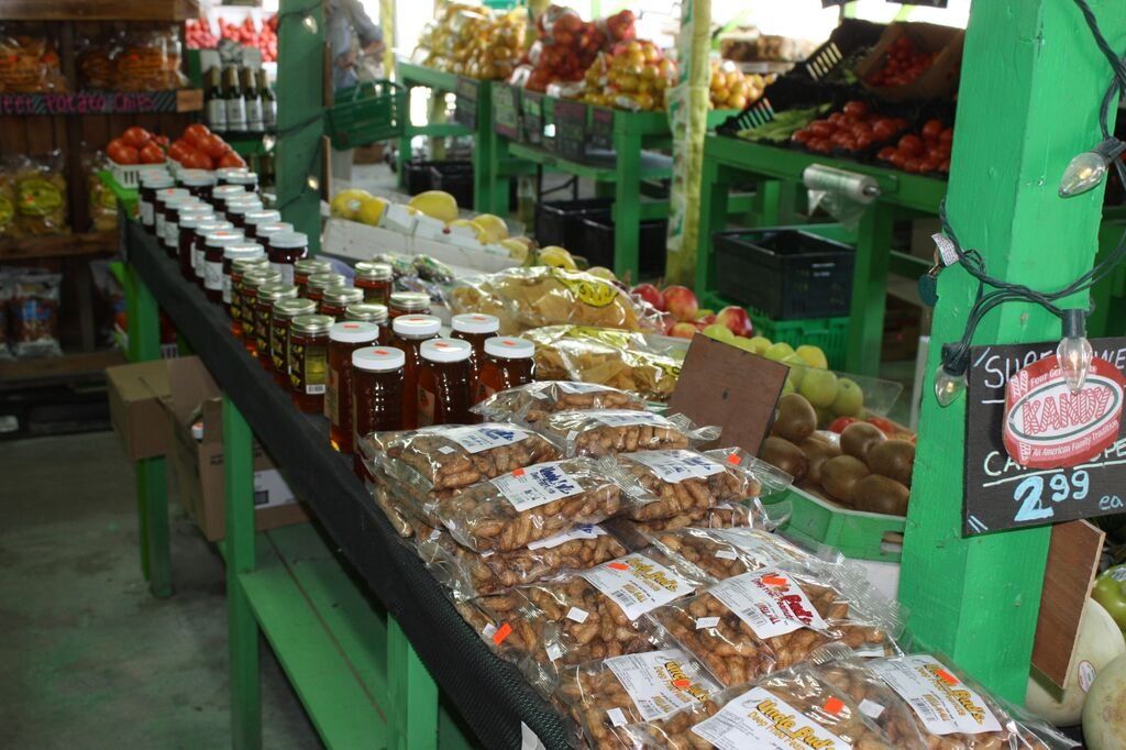 Produce stand with various goods: jars, snacks, fruits, and vegetables.