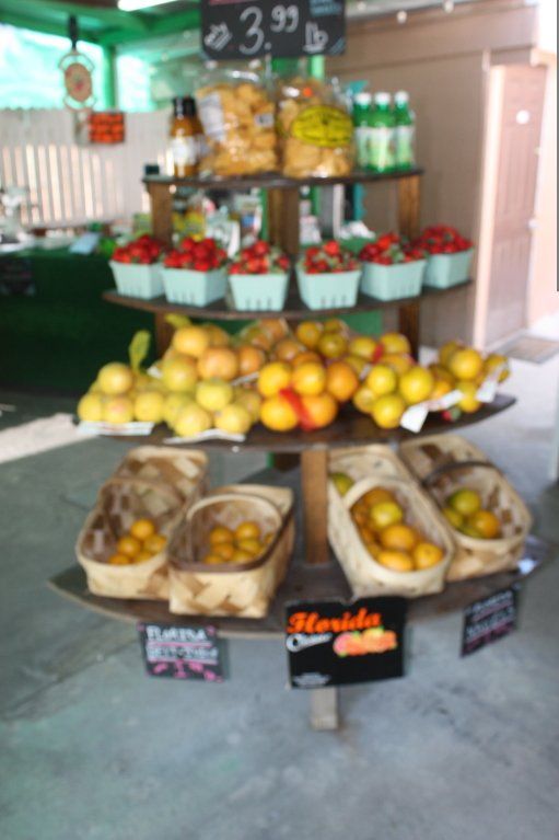 Farmers market display: strawberries, citrus, snacks, and drinks on tiered wooden shelves. Florida sign visible.
