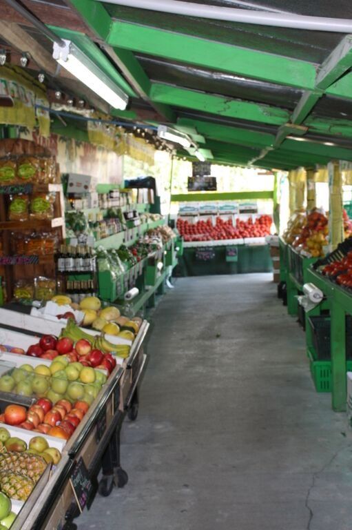 Produce market with various fruits and vegetables on display. Green painted stalls with open-air setting.
