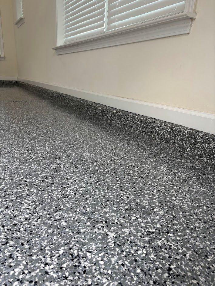 Epoxy flake flooring in a room with a window, white trim, and neutral-colored walls.