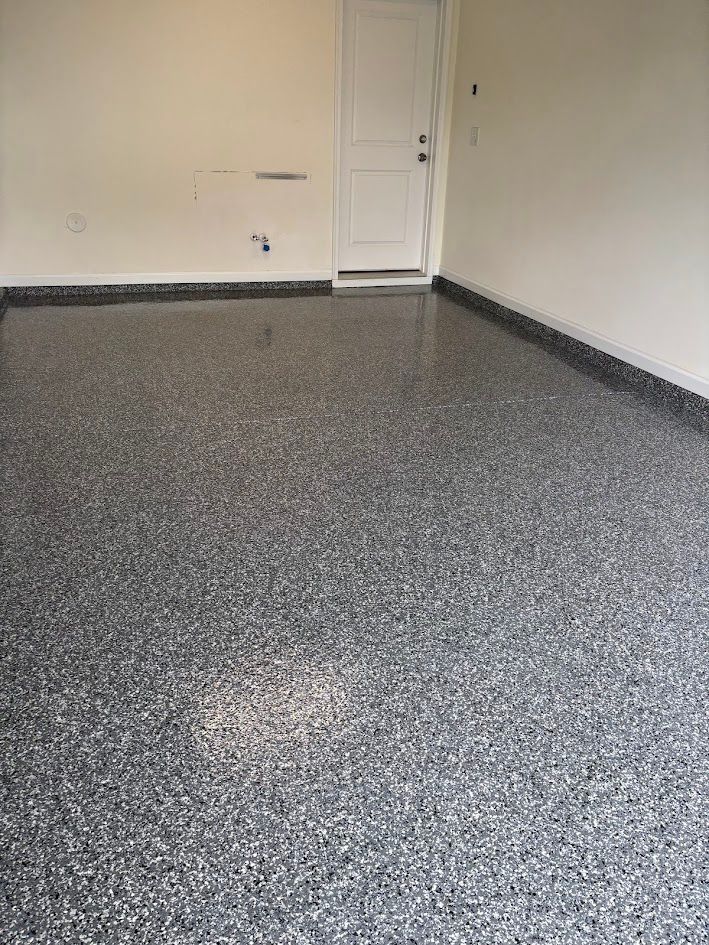 Garage interior with speckled gray epoxy floor. A white door is in the back. Beige walls.