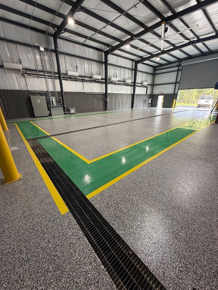 Inside a warehouse with a speckled floor, a large green area with yellow borders surrounds a drainage grate.
