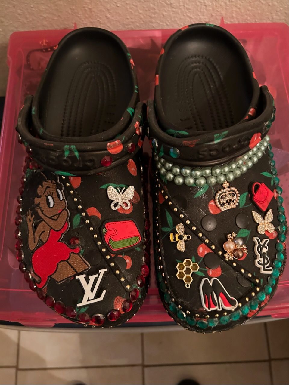 Black Crocs decorated with various charms, including jewels, a cartoon figure, and a Louis Vuitton logo.