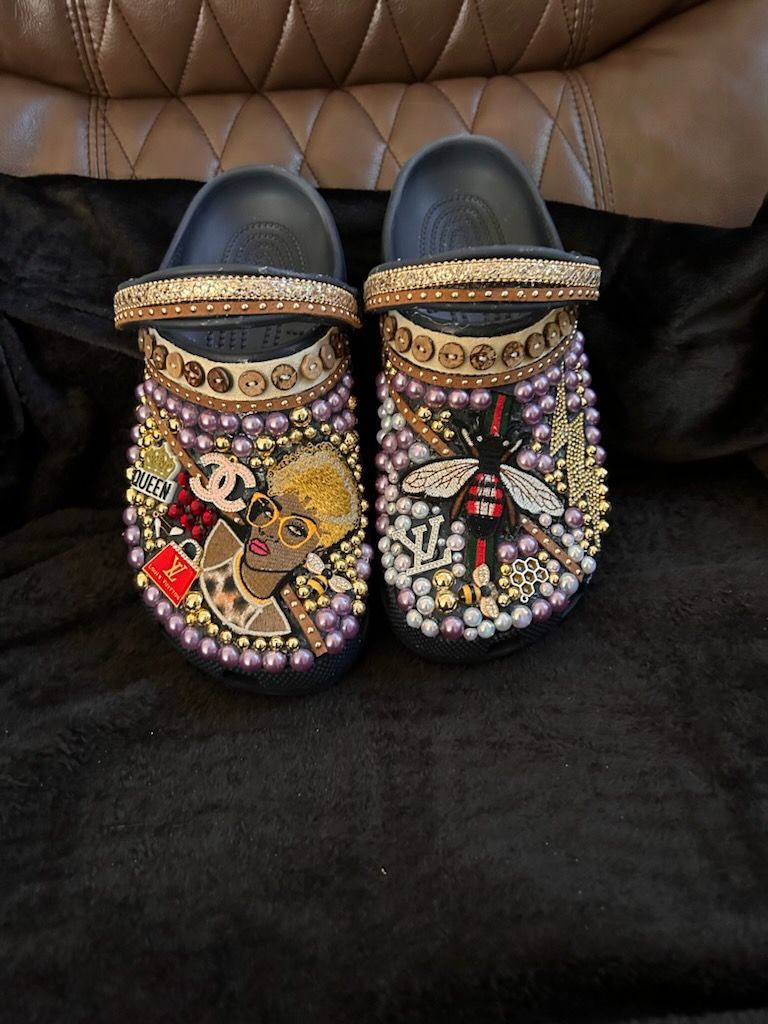 Customized black Crocs with pearl, bead, and gem embellishments, featuring brand logos and illustrations.