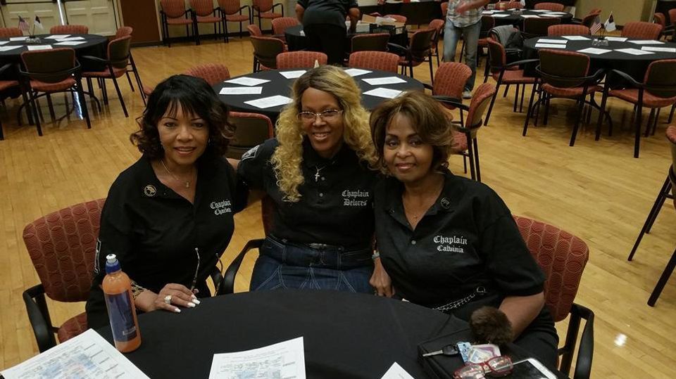 Three women in black shirts smiling at a table in a room with tables and chairs.