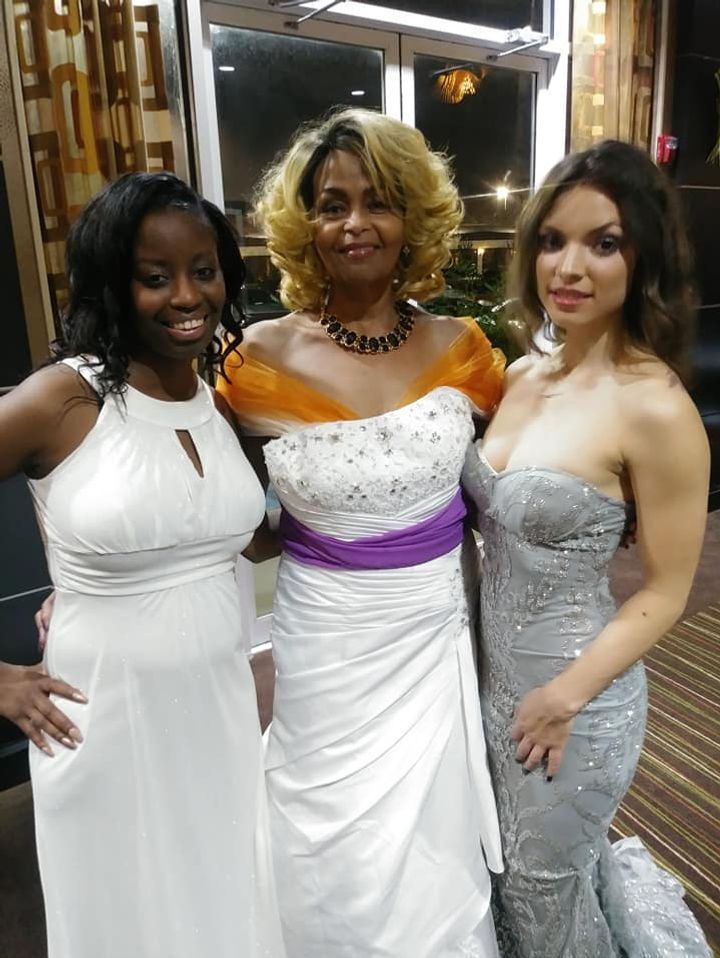Three women in formal dresses pose together indoors.