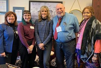 Five people standing together, smiling. Indoor setting with art and a mirror.