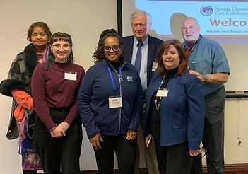 Group of people in front of a welcome banner, smiling at the camera. Indoor setting.