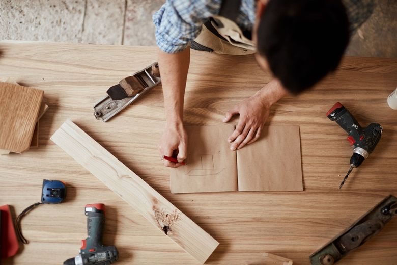 Carpenter drawing on paper on a wooden workbench, surrounded by tools.
