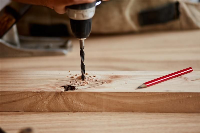 Drill boring into wood, sawdust, pencil lies next to it.