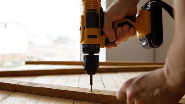 A person drilling a screw into a wooden board with a yellow and black power drill.