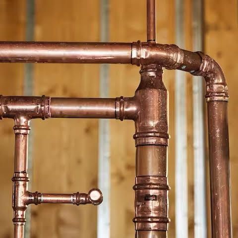 Copper plumbing pipes with various joints against a wooden and metal background.