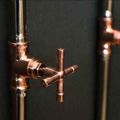 Copper plumbing pipes with a cross-shaped valve against a dark background.