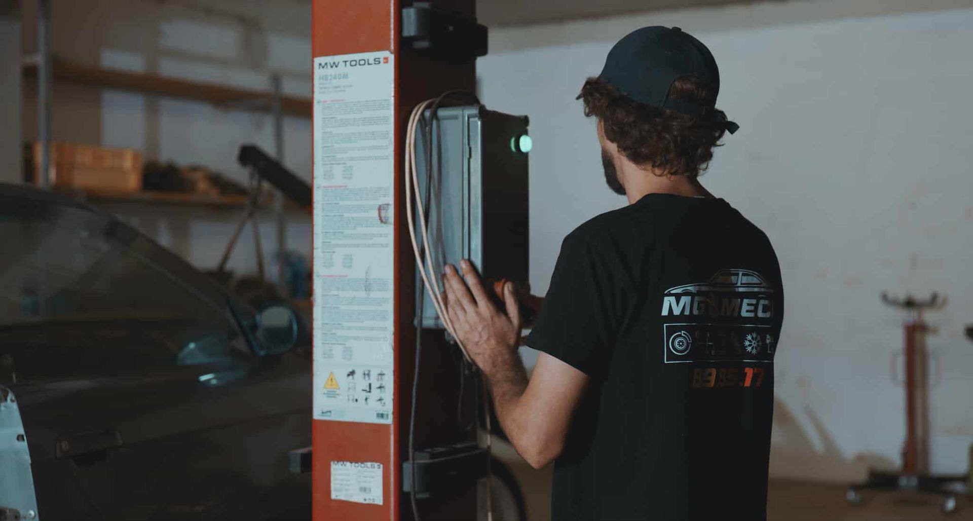 Man in black shirt operates a control panel on a car lift in a garage.