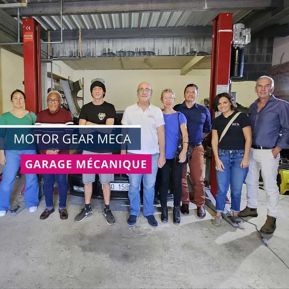 Group of people in a garage posing in front of a car lift. Banner reads 