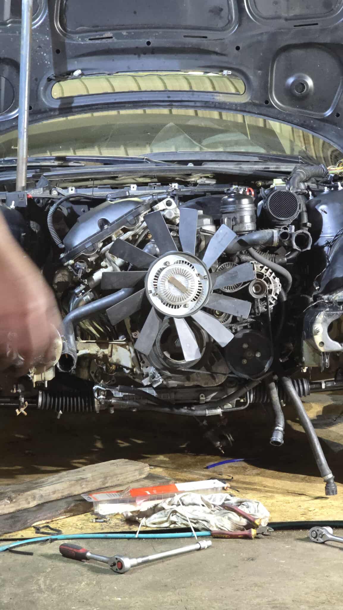 Car engine being worked on with open hood. Tools and parts are visible.