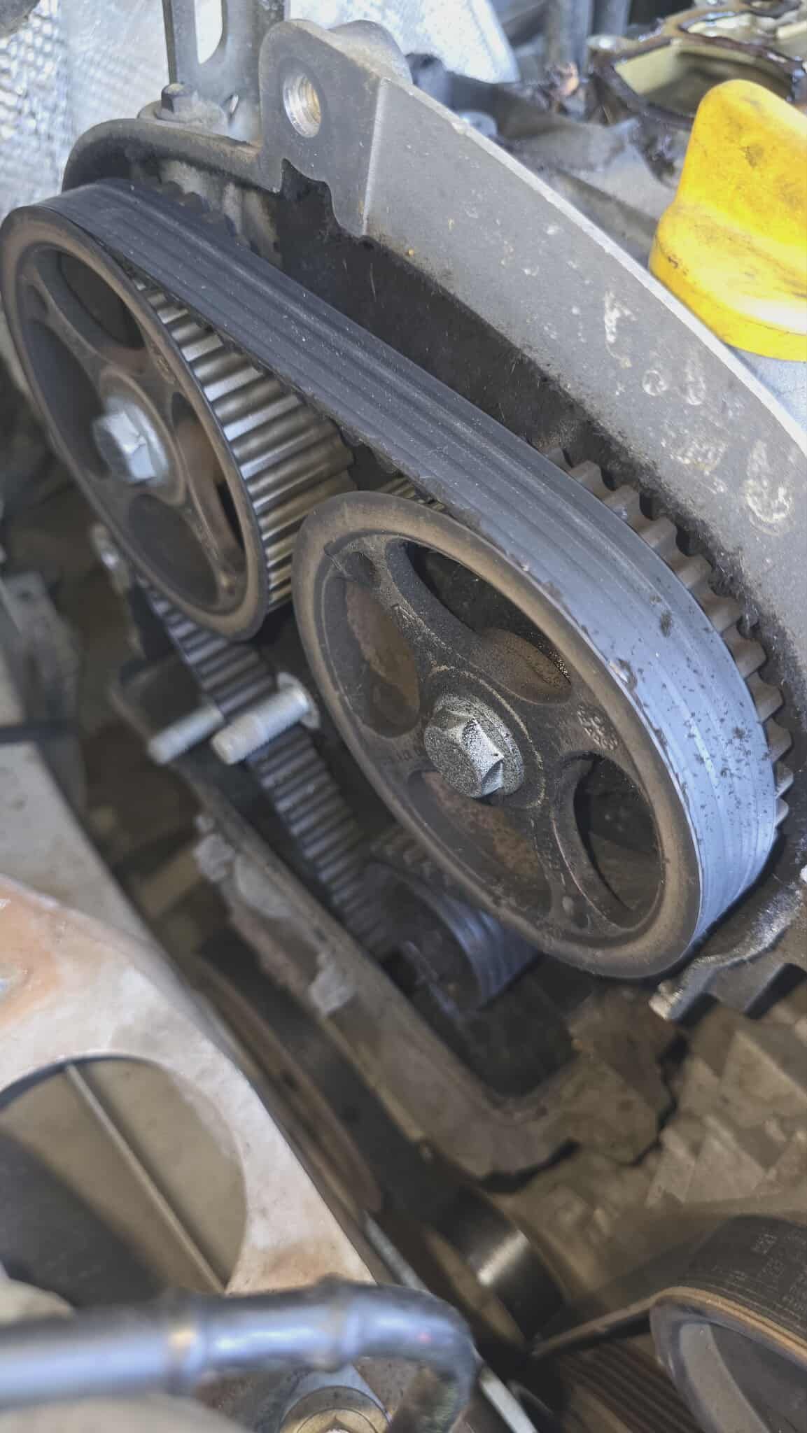 Close-up of a car engine's timing belt and pulleys, showing wear and tear.