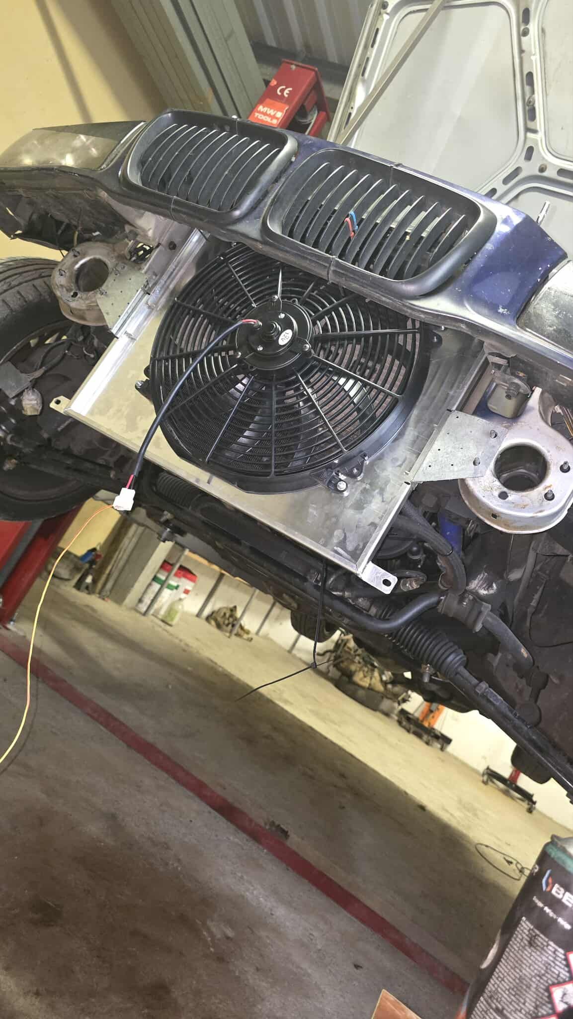 Silver fan and radiator installed on a car in a garage.