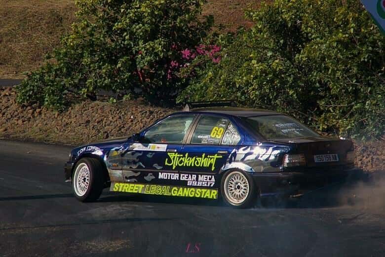 Blue car drifting on asphalt track, smoke billowing from tires.