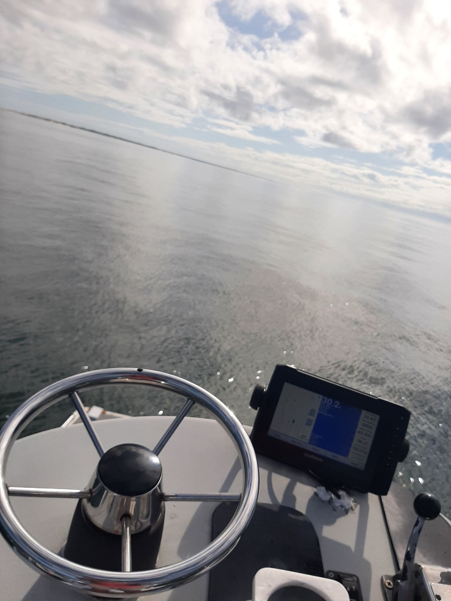 Steering wheel and navigation screen on a boat. Ocean and sky in the background.
