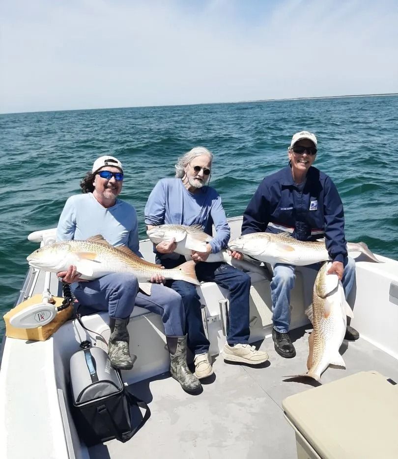 Three men on a boat hold up large redfish they caught on a sunny day at sea.