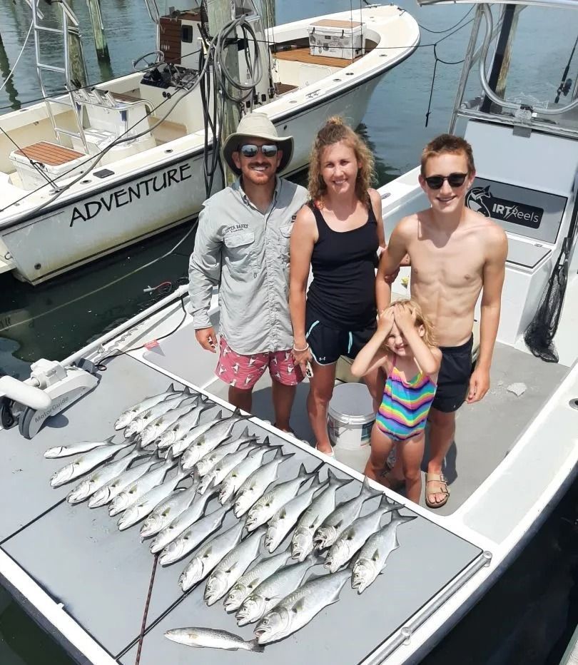 Family on a boat displaying a catch of fish. Smiling, sunny day.