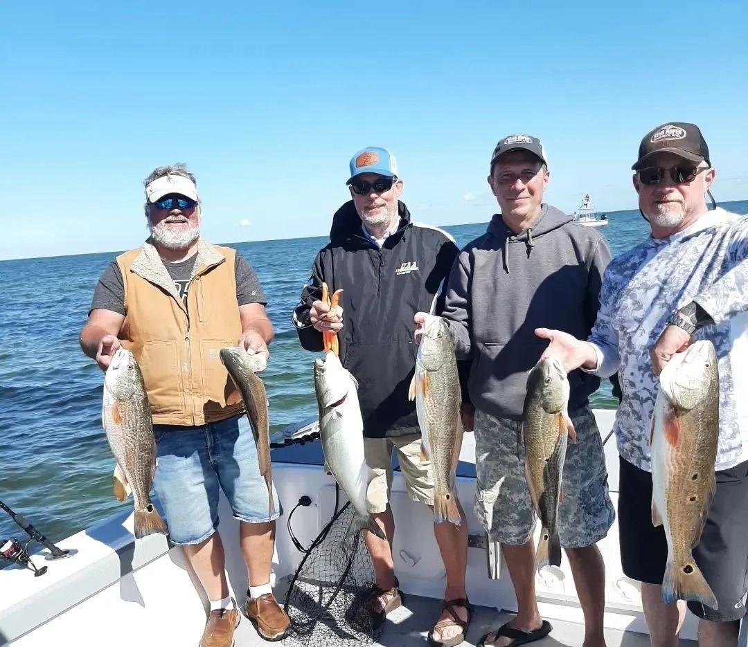 Four men on a boat holding fish they caught. Blue sky and water.