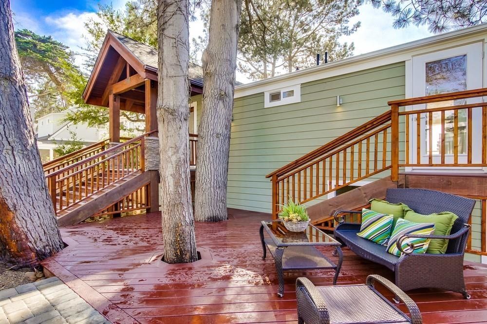 A wooden deck with a couch , chairs , table and stairs in front of a house.