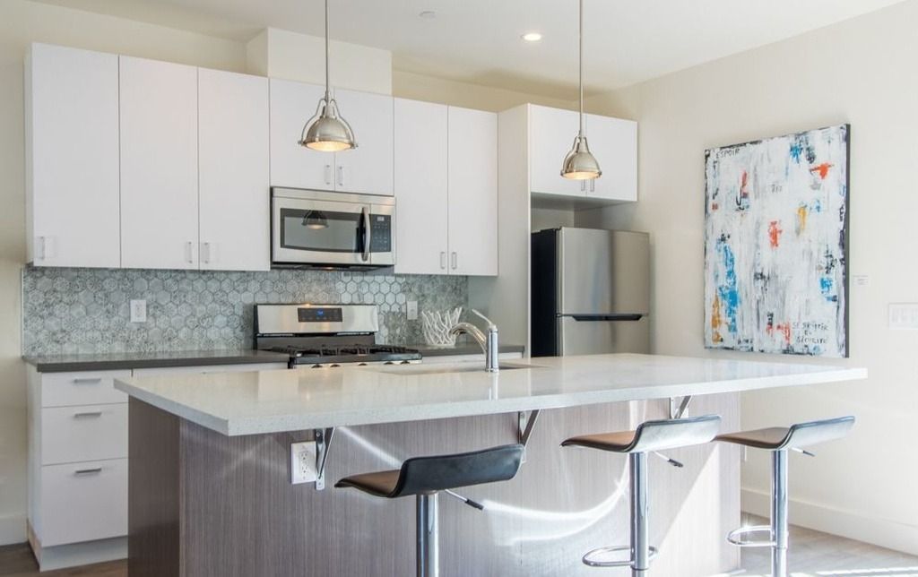 A kitchen with white cabinets , stainless steel appliances , and a large island.