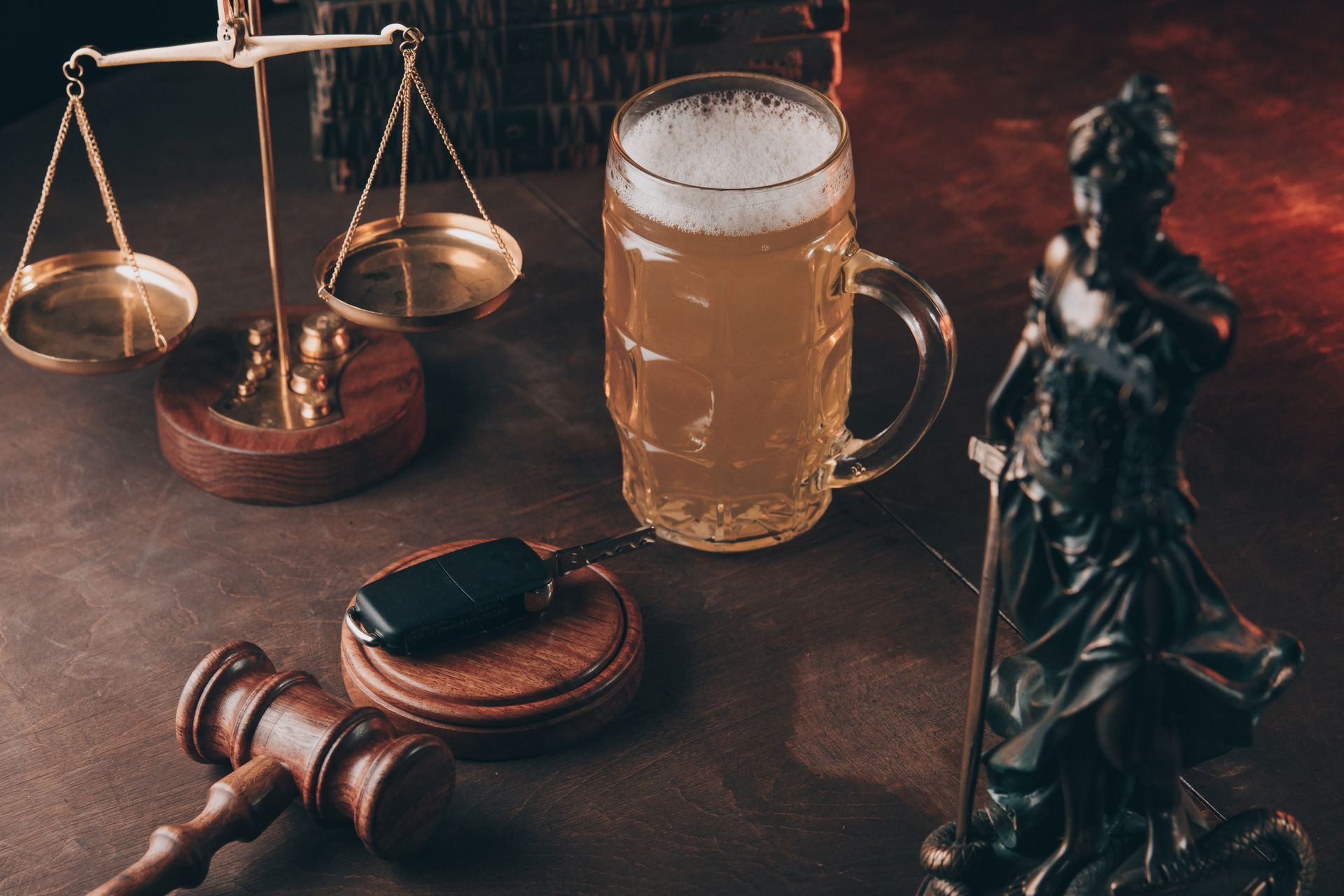 Scales, gavel, beer mug, car keys, and Lady Justice statue on a brown surface, suggesting legal and drinking themes.