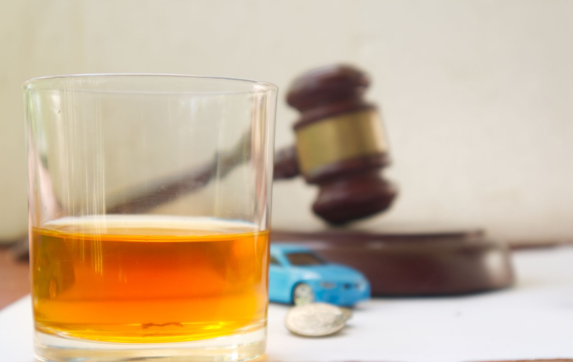 Glass of amber liquid with gavel and toy car, hinting at DUI and legal issues. Glass of amber liquid with gavel and toy car, hinting at DUI and legal issues.