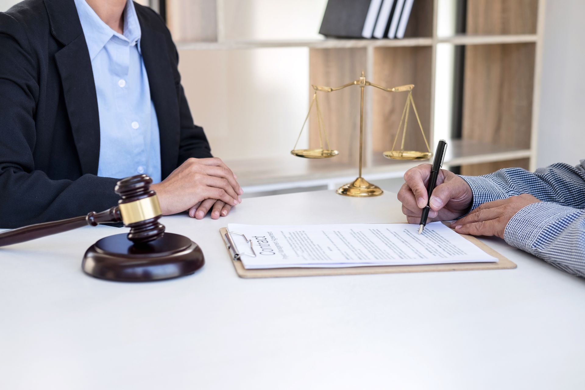 Person signing a document in a legal setting, scales of justice, gavel on the table.