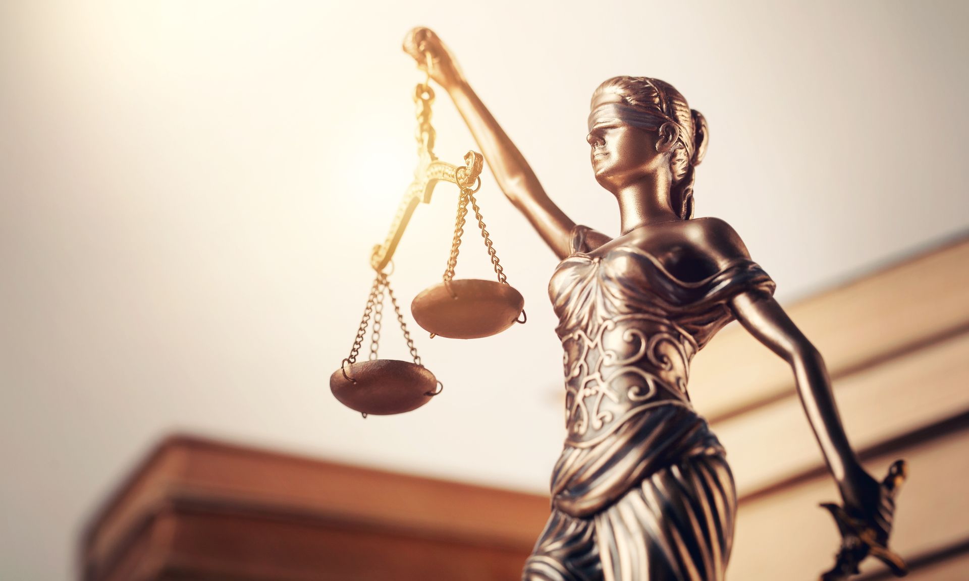 Statue of Lady Justice holding scales, gold and bronze with sunlight and books.